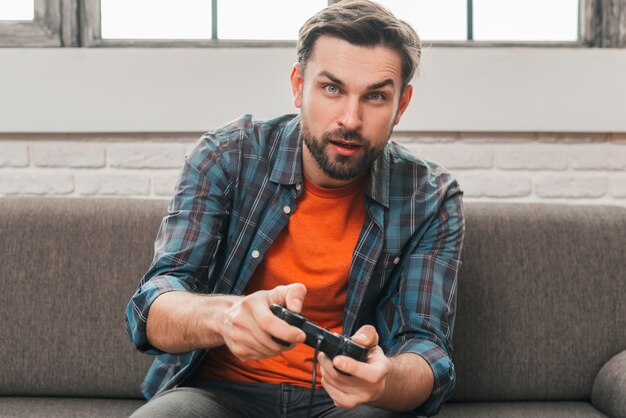Портрет молодого человека, сидящего на диване и играющего в видеоигру
