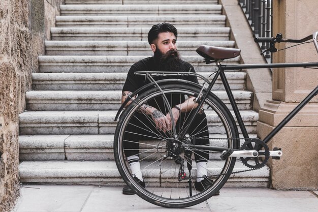 Portrait of a young man sitting on staircase with bicycle