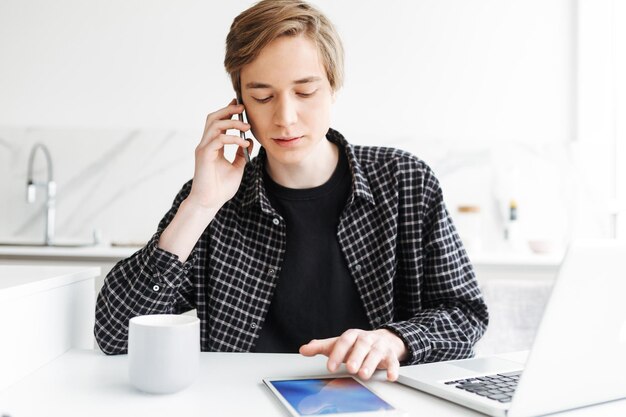 自宅のキッチンで彼の携帯電話に座って話している若い男の肖像画