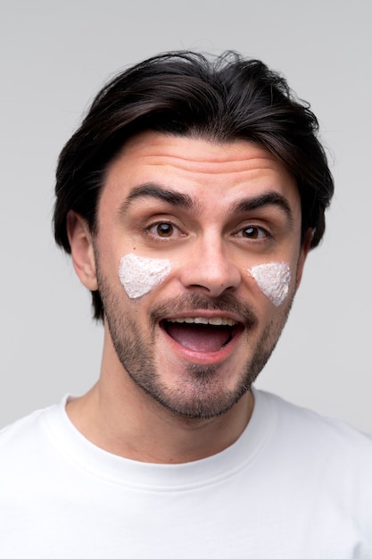 Портрет улыбающегося молодого человека с увлажняющим кремом на щеках
