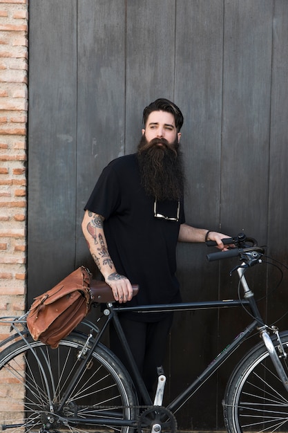 Portrait of a young man standing with bicycle in front of closed black door