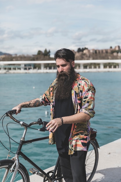 海岸近くの自転車で立っている若い男の肖像