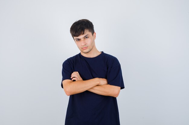 Portrait of young man standing with crossed arms in black t-shirt and looking serious front view