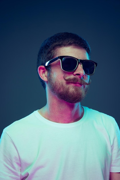 Portrait of young man in stylish sunglasses isolated over blue studio background in neon light
