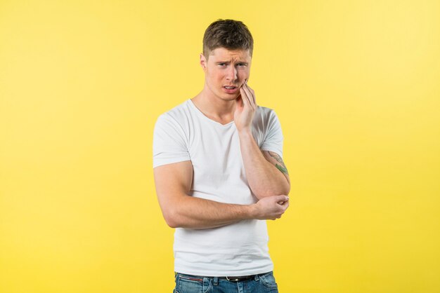 Portrait of a young man suffering from toothache against yellow background