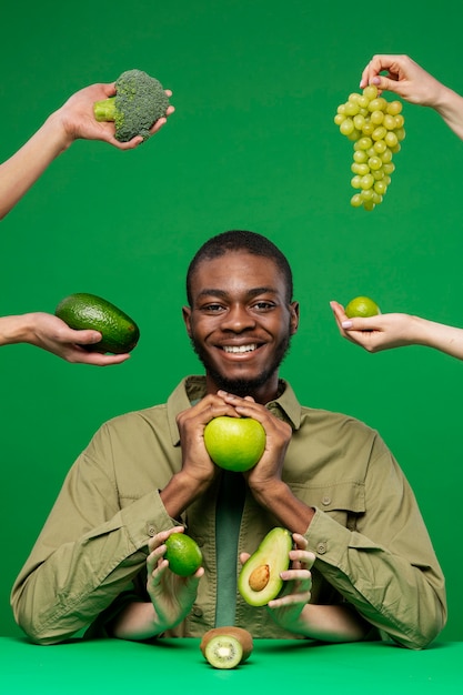 Portrait of young man surrounded by hands with green fruit and broccoli