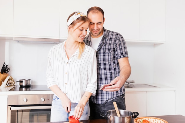 Портрет молодого человека, принимая селфи на мобильном телефоне с ее жена нарезка овощей с ножом
