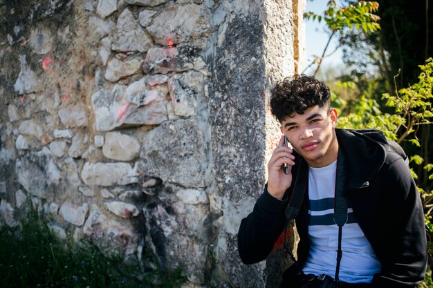 Портрет молодого человека разговаривает по мобильному телефону возле каменной стены