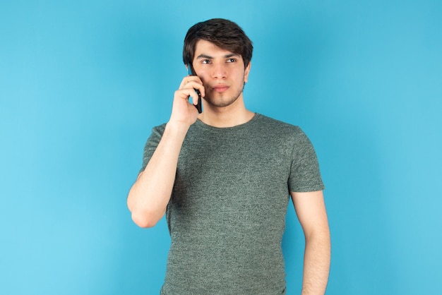 Портрет молодого человека разговаривает по мобильному телефону против синего цвета.