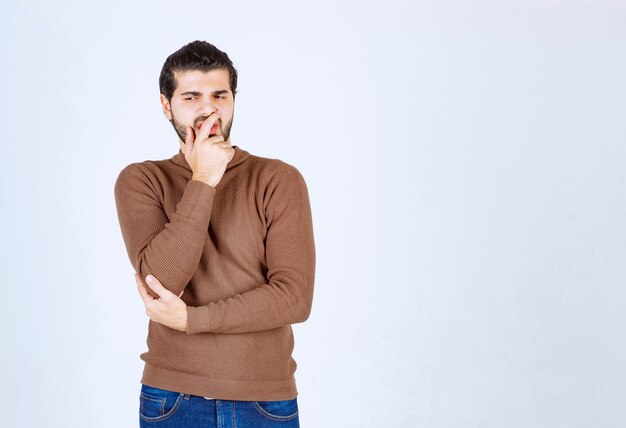 Portrait of a young man thinking and standing against white wall.