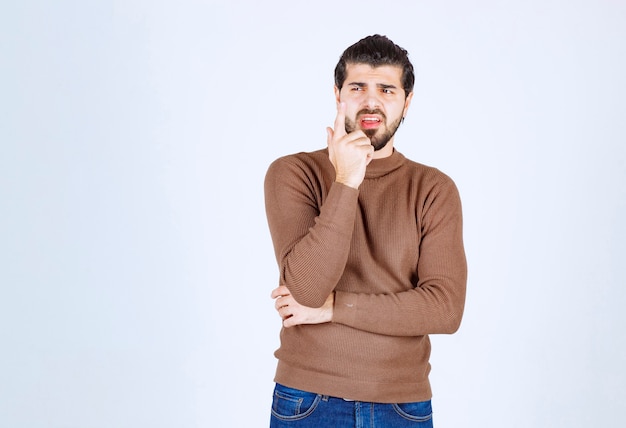 Portrait of a young man thinking and standing against white wall.