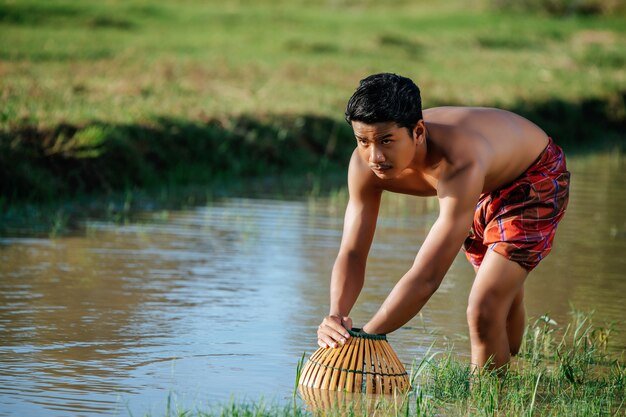肖像画トップレスの若い男は、料理のために魚を捕まえるために竹の釣り罠を使用します