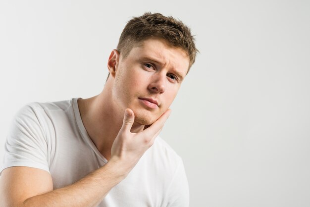 Portrait of a young man touching his face against white background