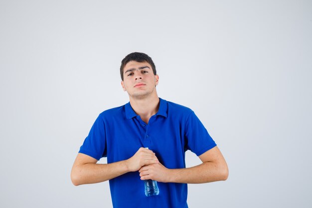 Portrait of young man trying to open plastic bottle in t-shirt and looking confident front view