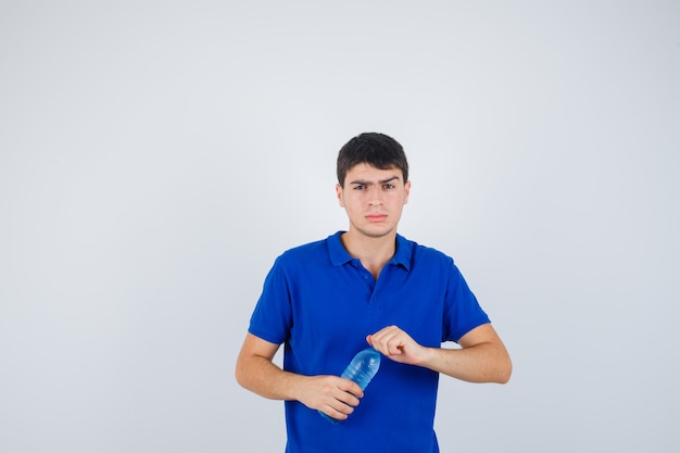 Portrait of young man trying to open plastic bottle in t-shirt and looking hesitant front view