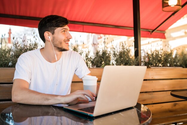 커피 숍에 앉아있는 동안 자신의 노트북을 사용하는 젊은 남자의 초상화. 기술 및 라이프 스타일 개념.