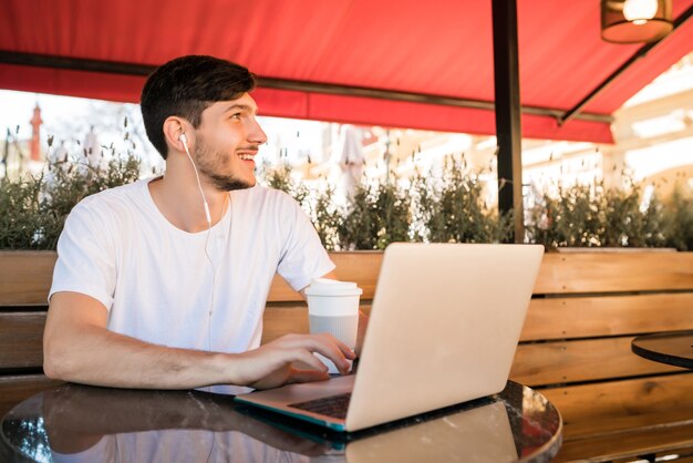 コーヒーショップに座っているときに彼のラップトップを使用して若い男の肖像画。テクノロジーとライフスタイルのコンセプト。