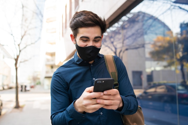 Portrait of young man using his mobile phone while walking outdoors on the street. New normal lifestyle concept. Urban concept.