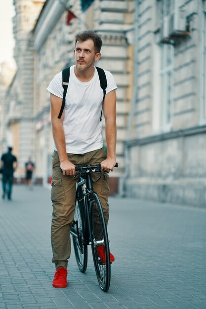 Portrait of young man walking with thoughtfully classic bicycle on city streets