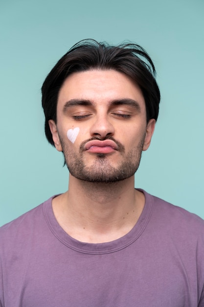 Portrait of a young man wearing a heart on his face made of moisturizer