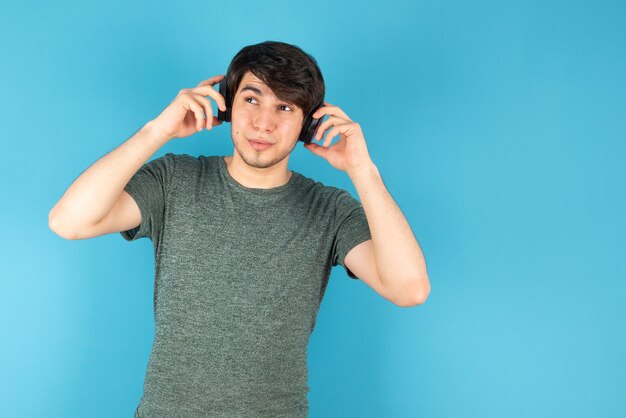 Portrait of young man with headphones on head against blue .