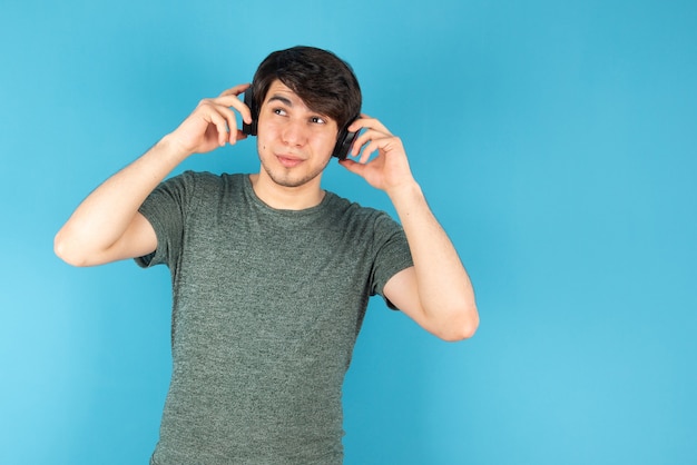 Portrait of young man with headphones on head against blue .