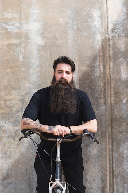 Portrait of a young man with long bearded sitting in front of concrete backdrop