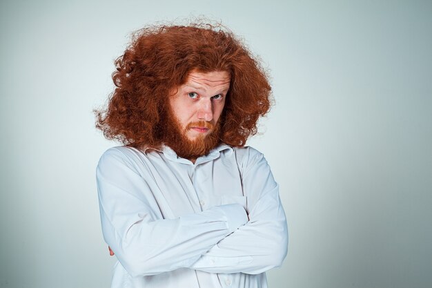 Portrait of young man with long red hair and with shocked facial expression on gray background