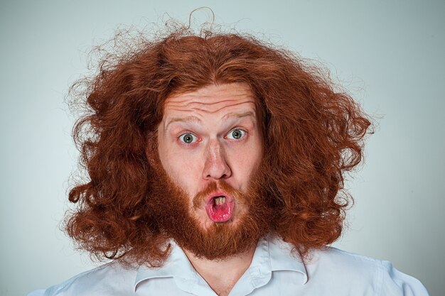 Портрет молодого человека с длинными рыжими волосами и шокированным выражением лица на сером фоне