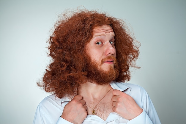 Free photo portrait of young man with long red hair and with shocked facial expression on gray background