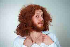 Free photo portrait of young man with long red hair and with shocked facial expression on gray background