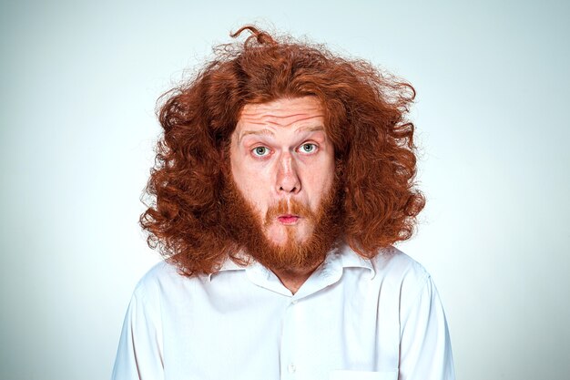 Портрет молодого человека с длинными рыжими волосами и шокированным выражением лица на сером фоне