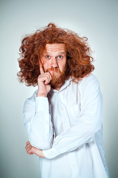 Free photo portrait of young man with long red hair and with shocked facial expression on gray background