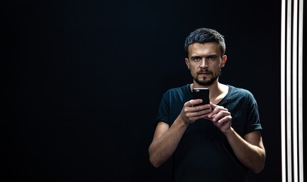 Portrait of a young man with a phone in his hands in the dark.