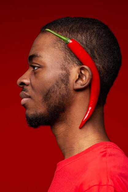 Portrait of young man with red chili pepper behind his year