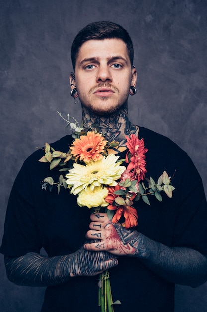 Портрет молодого человека с татуировкой и пирсингом в носу и ушах, держа в руке букет цветов