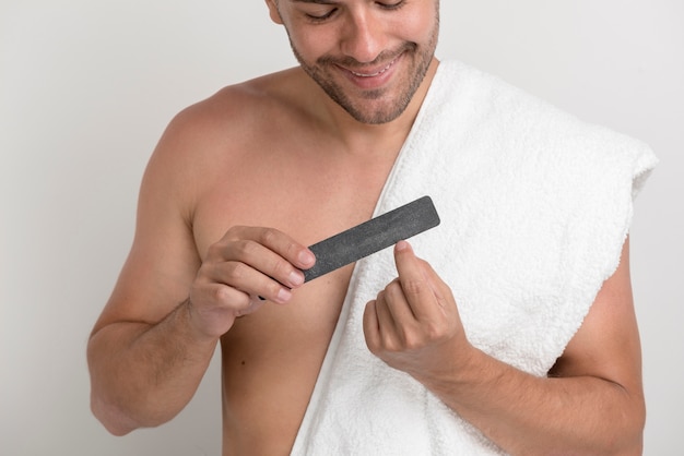 Portrait of young man with white towel polishing his nails with fine