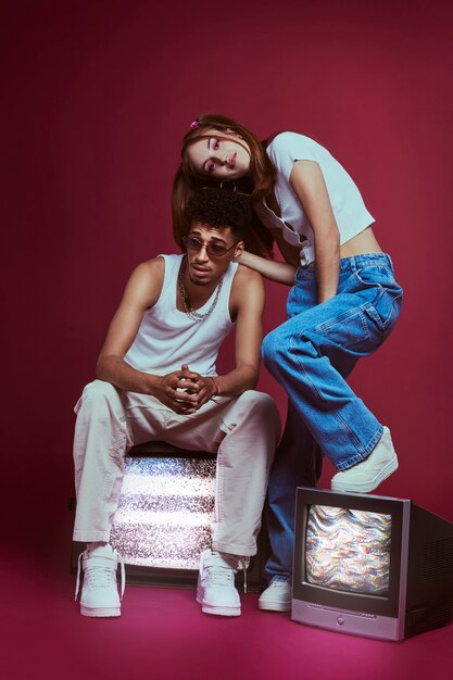 Portrait of young man and woman in 2000s fashion style posing with tv