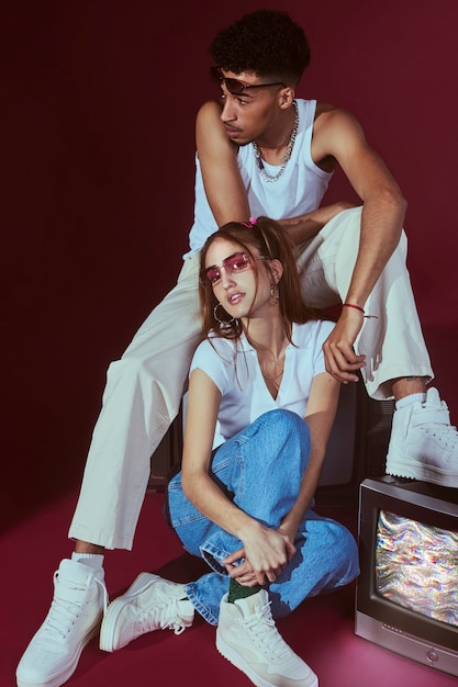 Free photo portrait of young man and woman in 2000s fashion style posing with tv