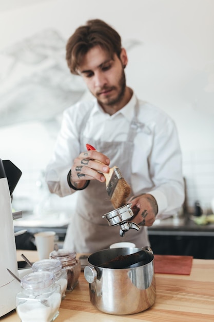 커피숍 바 카운터에서 일하는 젊은 남자의 초상화 앞치마를 입은 바리스타와 카페에서 커피를 준비하는 흰색 셔츠 레스토랑에서 바리스타로 일하는 소년
