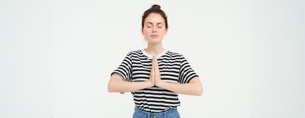 Free photo portrait of young mindful woman meditating holds hands clasped together namaste gesture practice