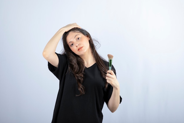 Portrait of young model with makeup with brushes standing on white wall. 