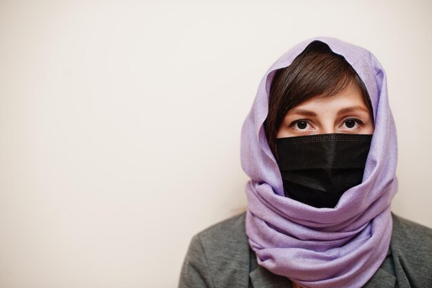 Portrait of young muslim woman wearing formal wear protect face mask and hijab head scarf against isolated background Coronavirus country concept