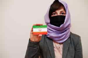 Free photo portrait of young muslim woman wearing formal wear protect face mask and hijab head scarf hold iran flag card against isolated background coronavirus country concept