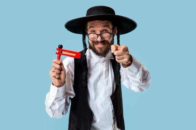 Portrait of a young orthodox jewish man with wooden grager ratchet during festival Purim. Holiday, celebration, judaism, tradition, religion concept.