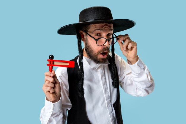 Portrait of a young orthodox jewish man with wooden grager ratchet during festival Purim