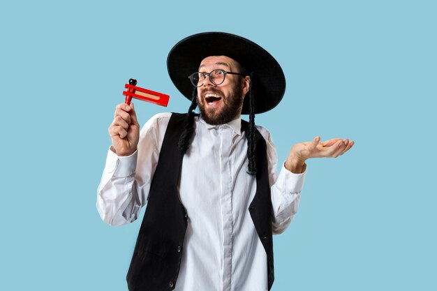 Portrait of a young orthodox jewish man with wooden grager ratchet during festival Purim