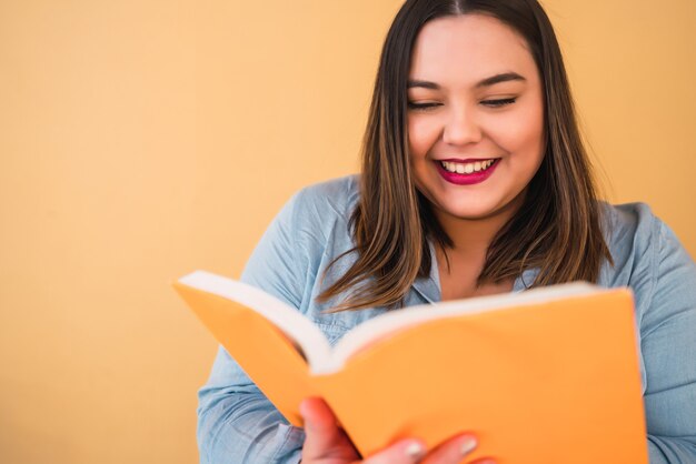 自由な時間を楽しんでいると黄色の空間に立ちながら本を読んで若いプラスのサイズの女性の肖像画。ライフスタイルのコンセプト。