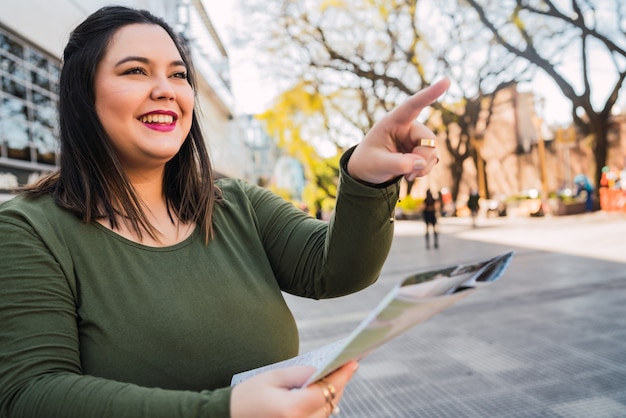 Portrait of young plus size woman holding a map and looking for directions outdoors in the street. Travel concept.