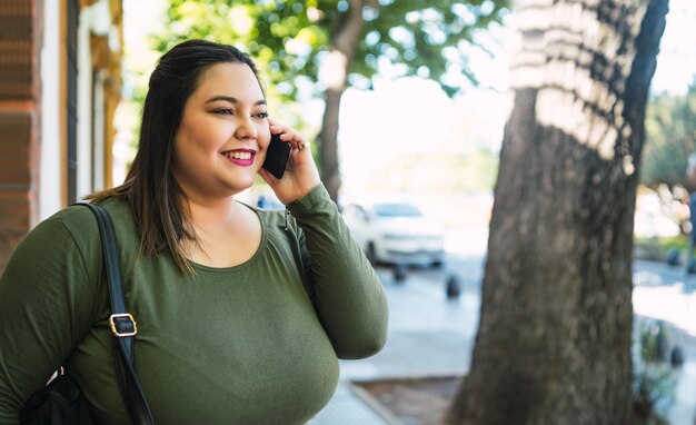 通りで屋外の電話で話しながら笑っている若いプラスのサイズの女性の肖像画。都市のコンセプト。